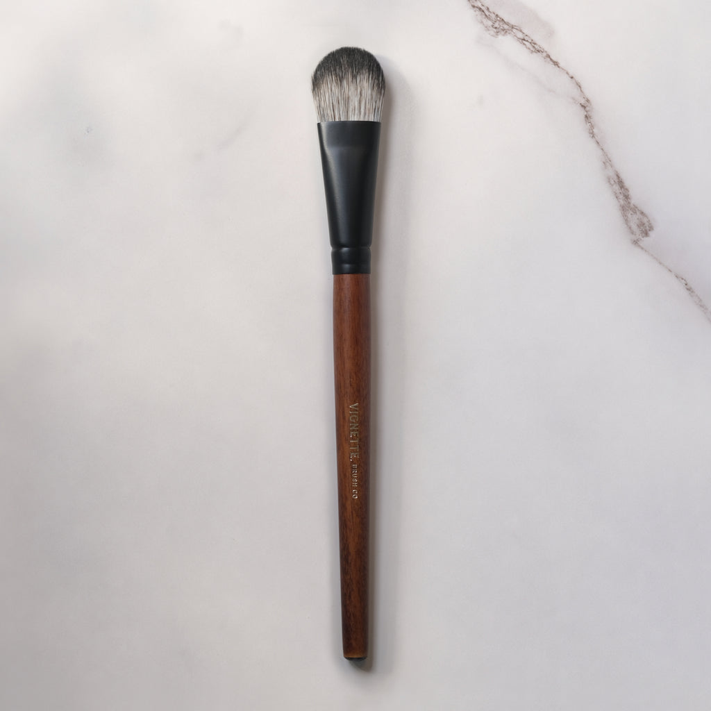 Makeup brush with wooden handle and black ferrule on a light gray background