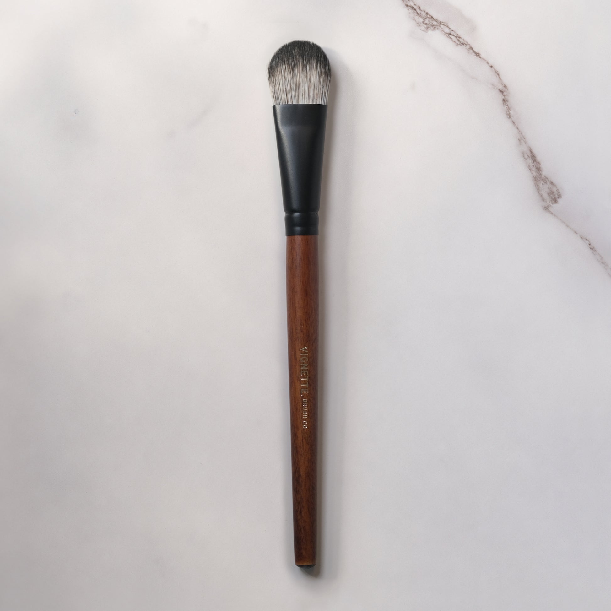 Makeup brush with wooden handle and black ferrule on a light gray background