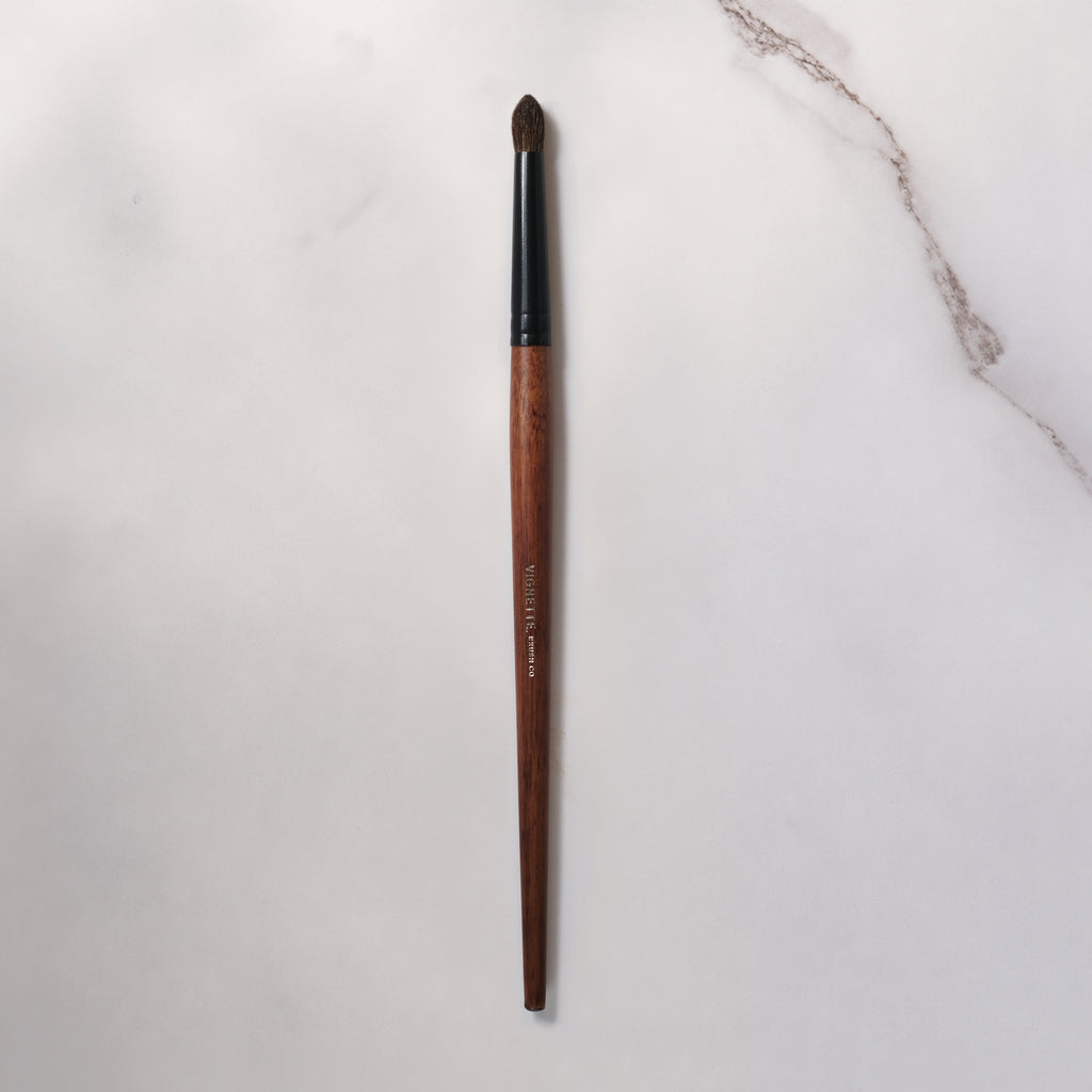 Makeup brush with wooden handle and black ferrule on a light gray background