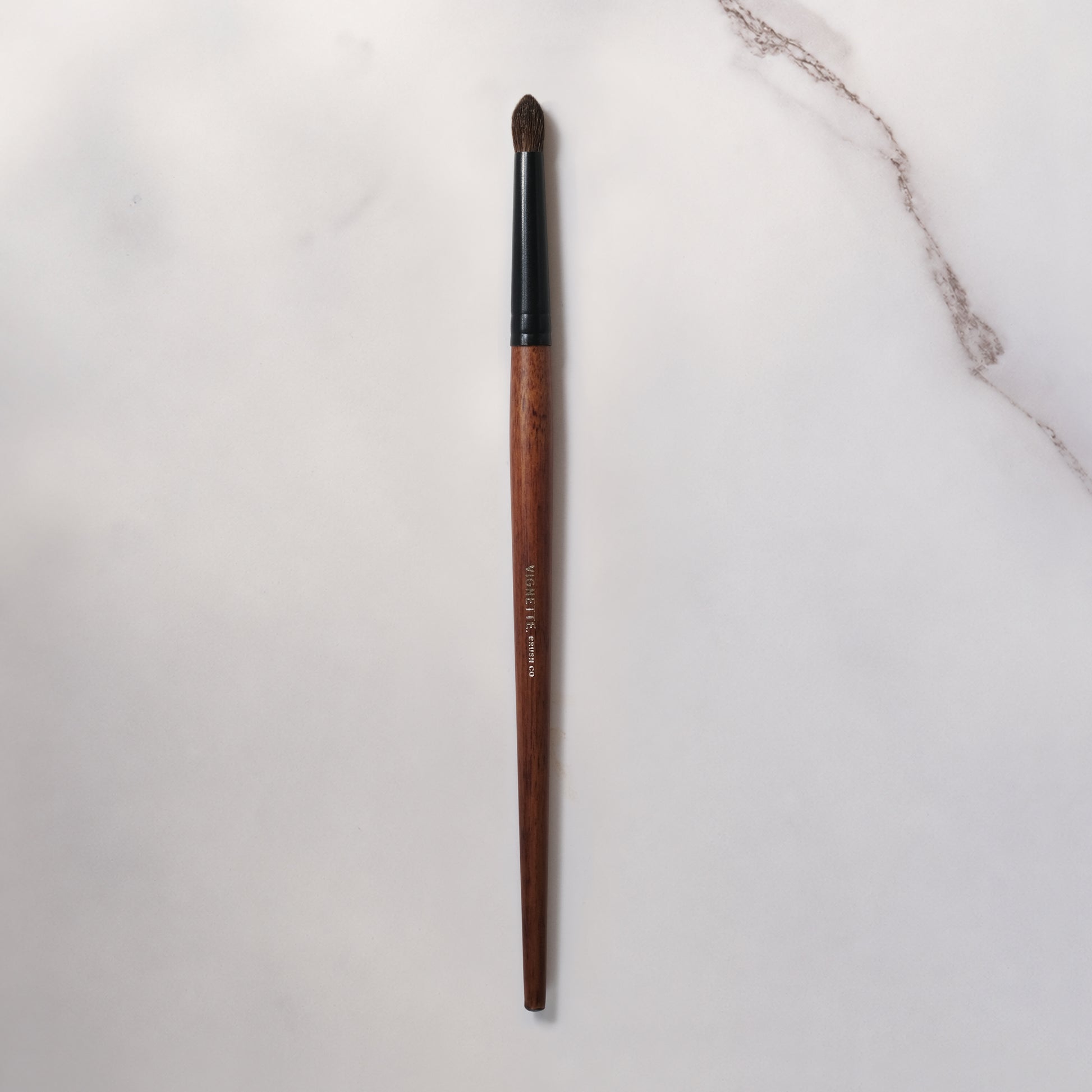 Makeup brush with wooden handle and black ferrule on a light gray background