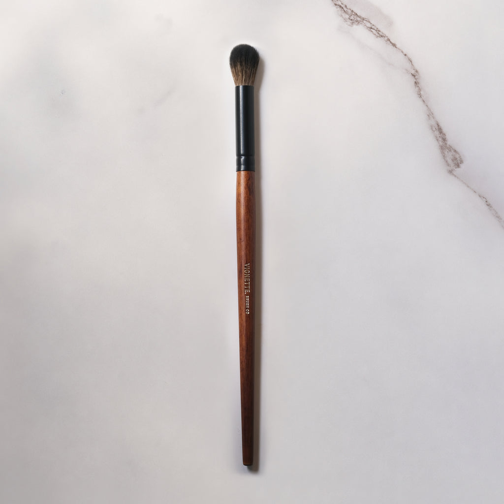 Makeup brush with brown handle and black ferrule on a light gray background