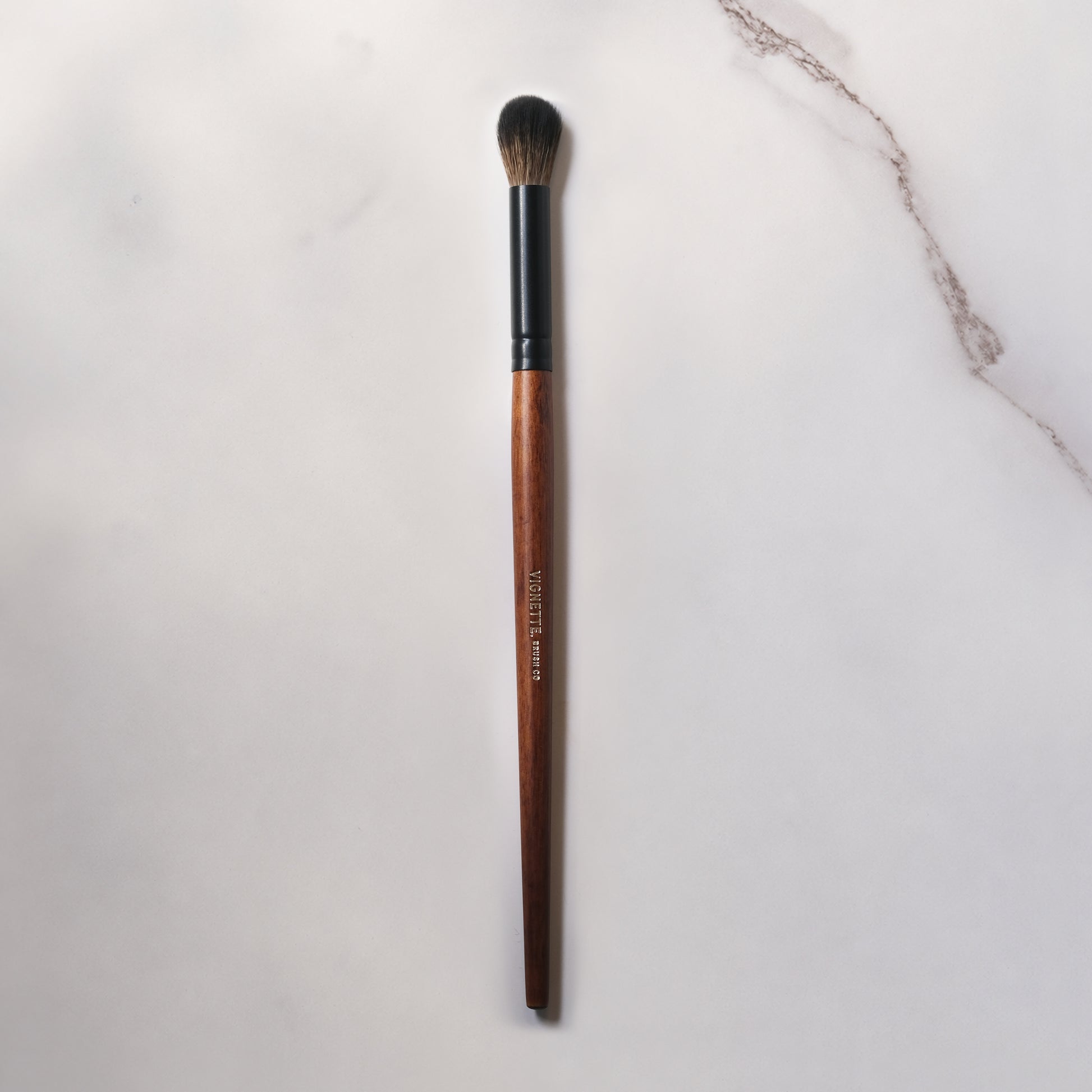 Makeup brush with brown handle and black ferrule on a light gray background