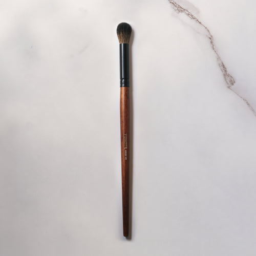 Makeup brush with brown handle and black ferrule on a light gray background