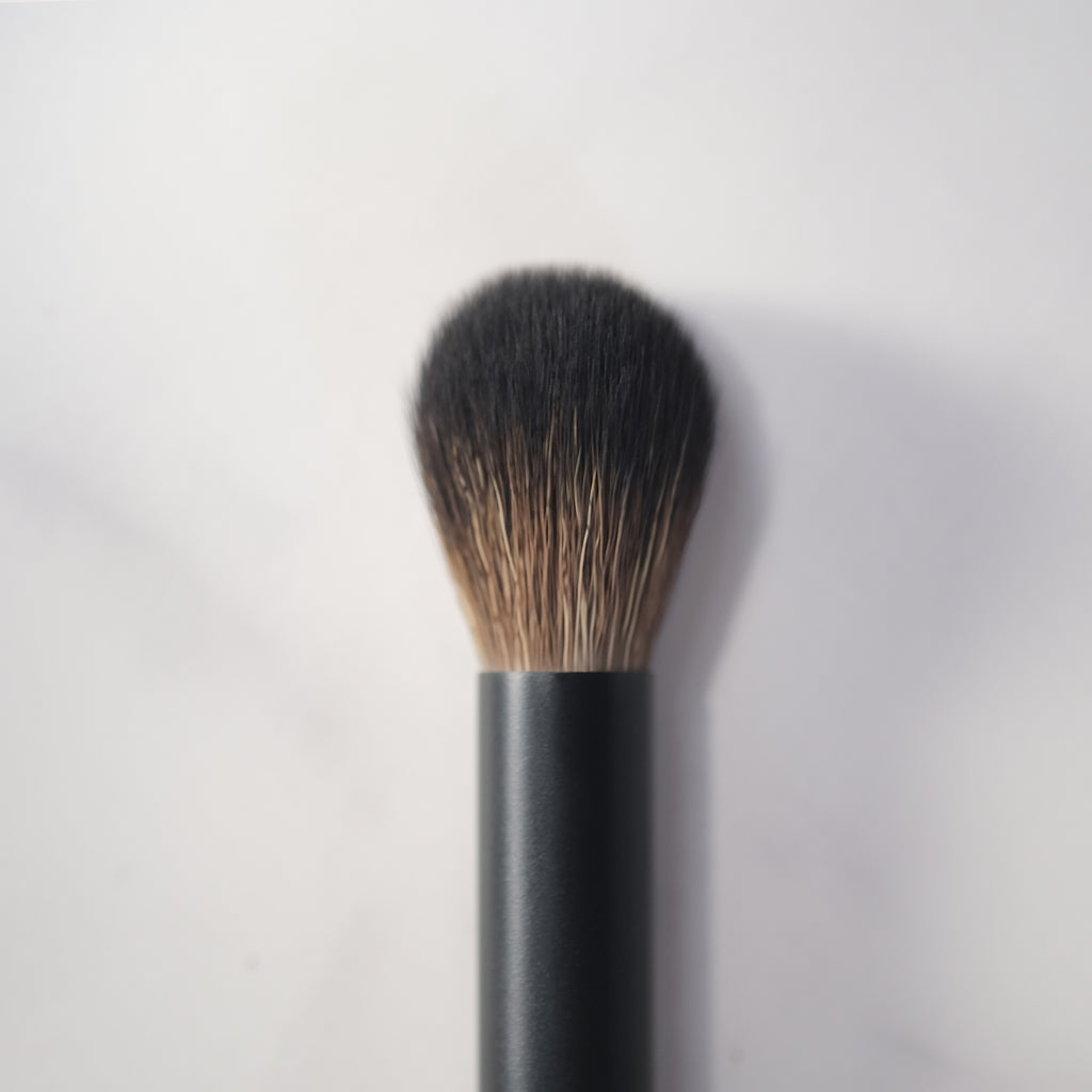 Makeup brush with black handle and bristles on a light gray background