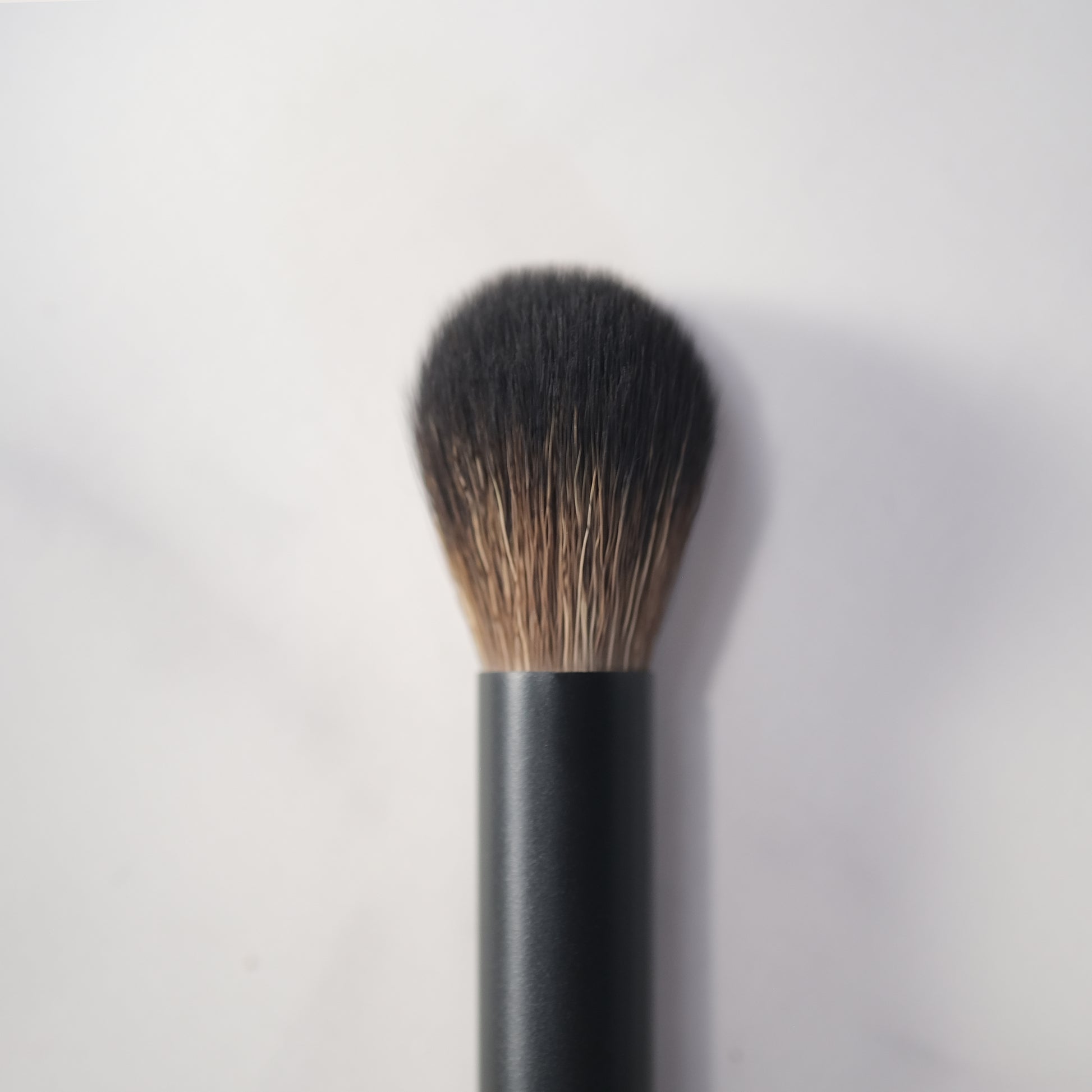 Makeup brush with black handle and bristles on a light gray background