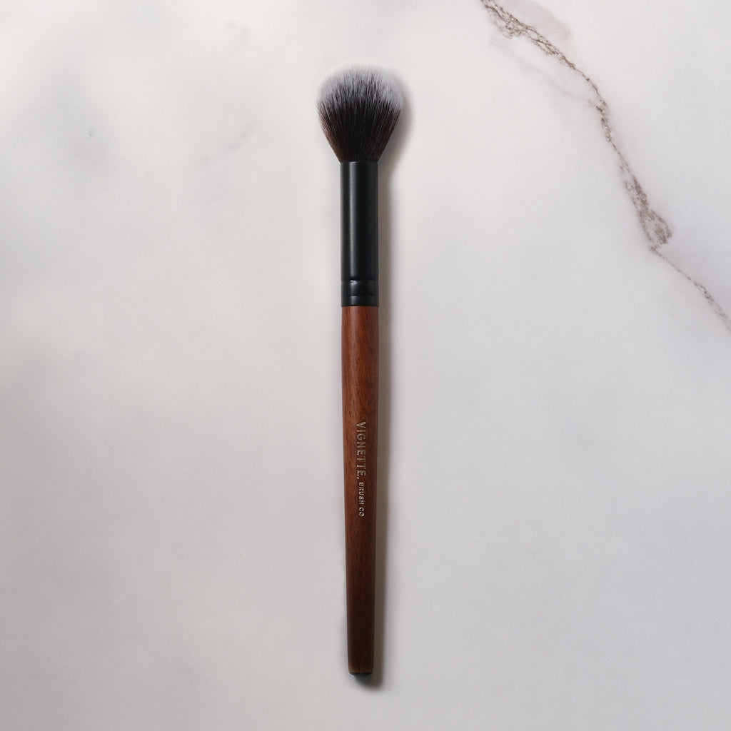 Makeup brush with brown handle and black ferrule on a light marble background