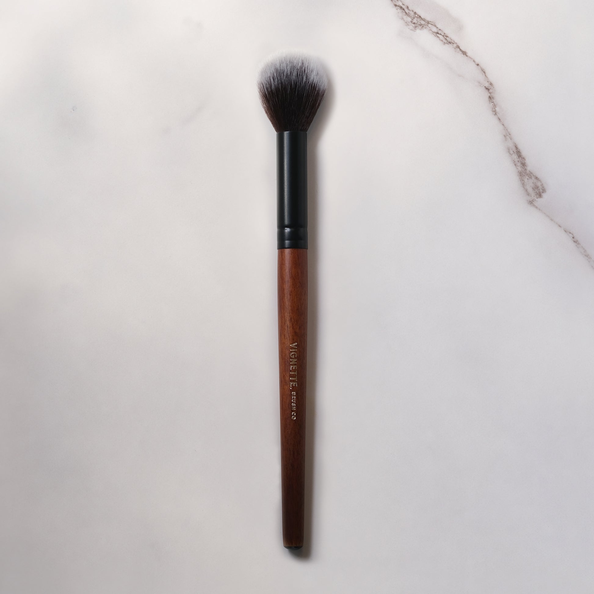 Makeup brush with brown handle and black ferrule on a light marble background