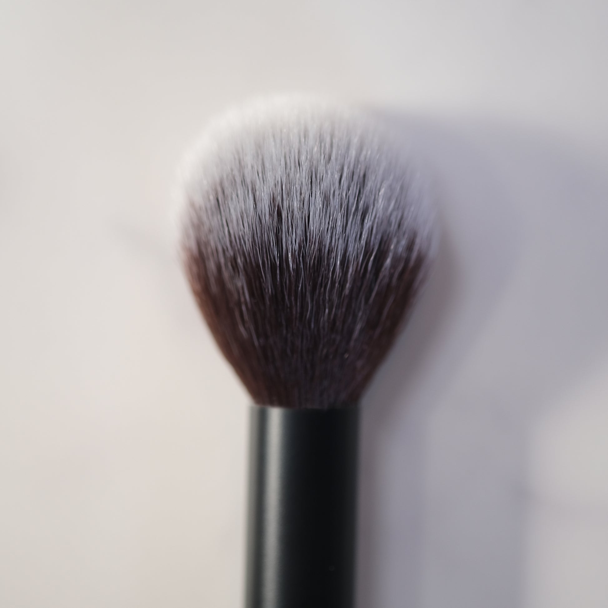 Makeup brush with black handle and white bristles on a light gray background