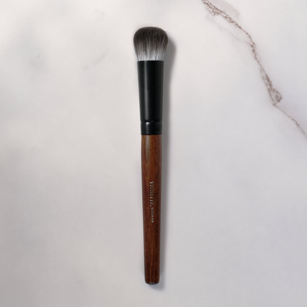 Makeup brush with wooden handle and black ferrule on a light gray background