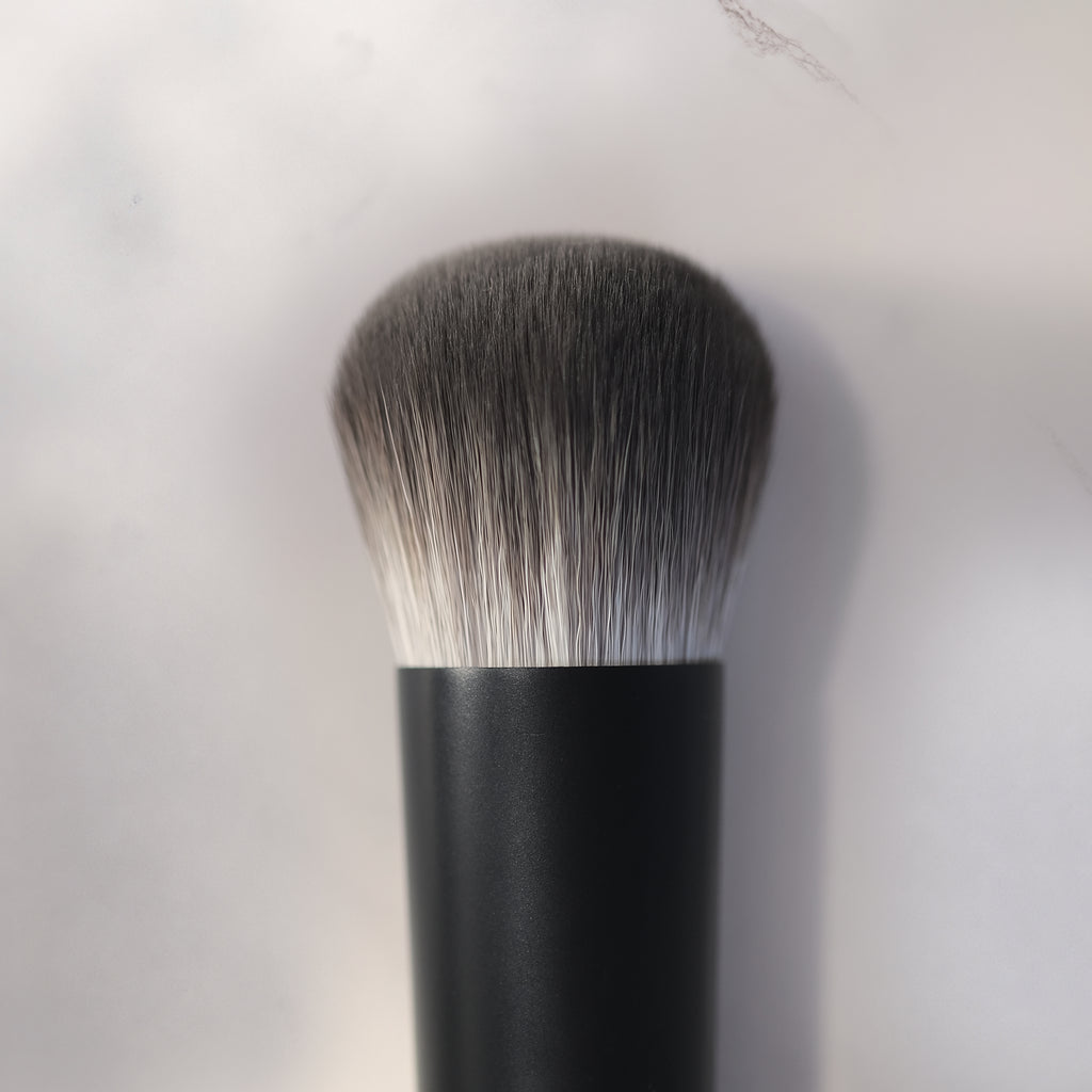 Makeup brush with black handle and gray bristles on a light gray background
