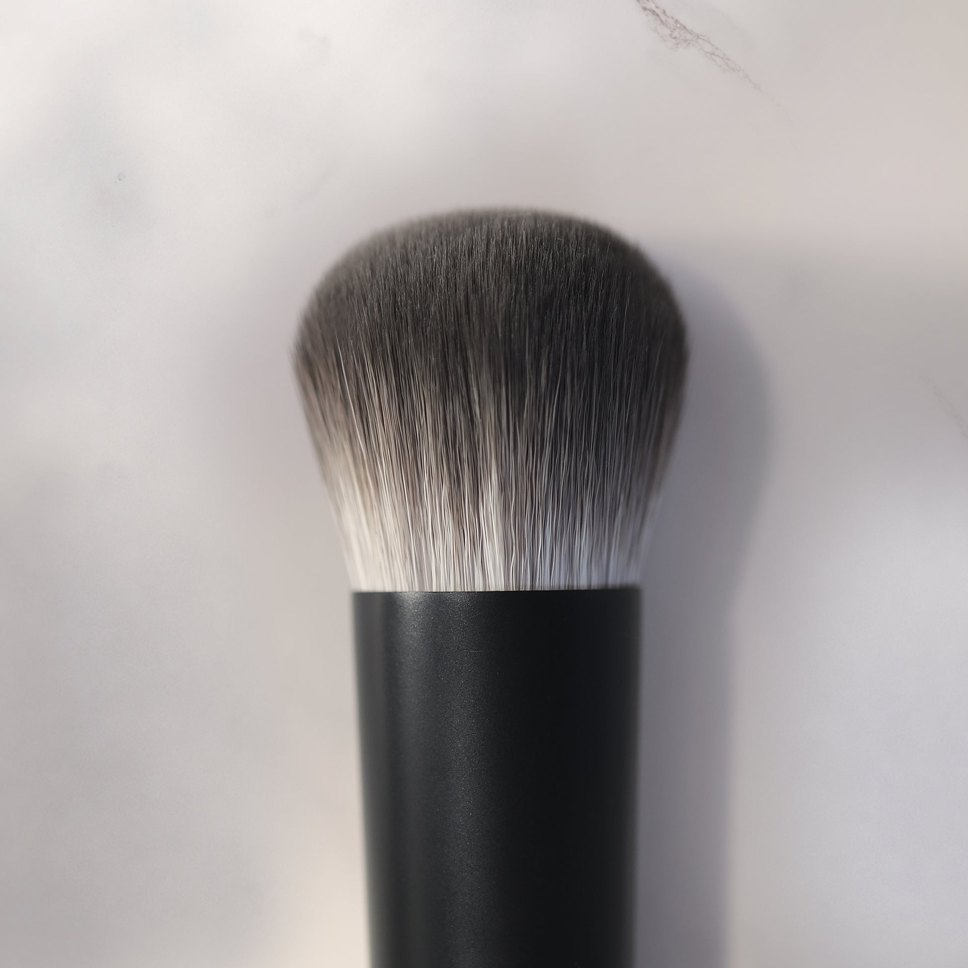 Makeup brush with black handle and gray bristles on a light gray background