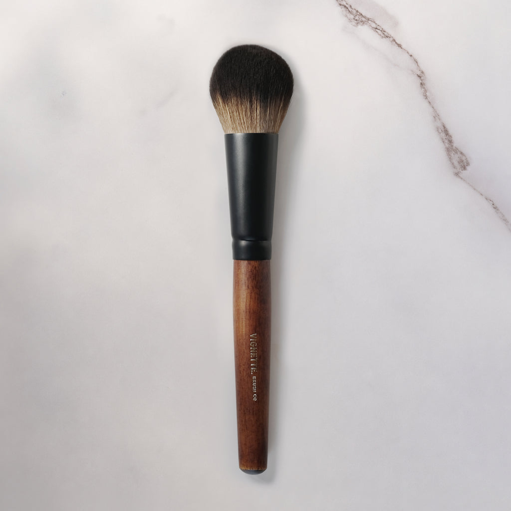 Makeup brush with wooden handle and black ferrule on a light gray background
