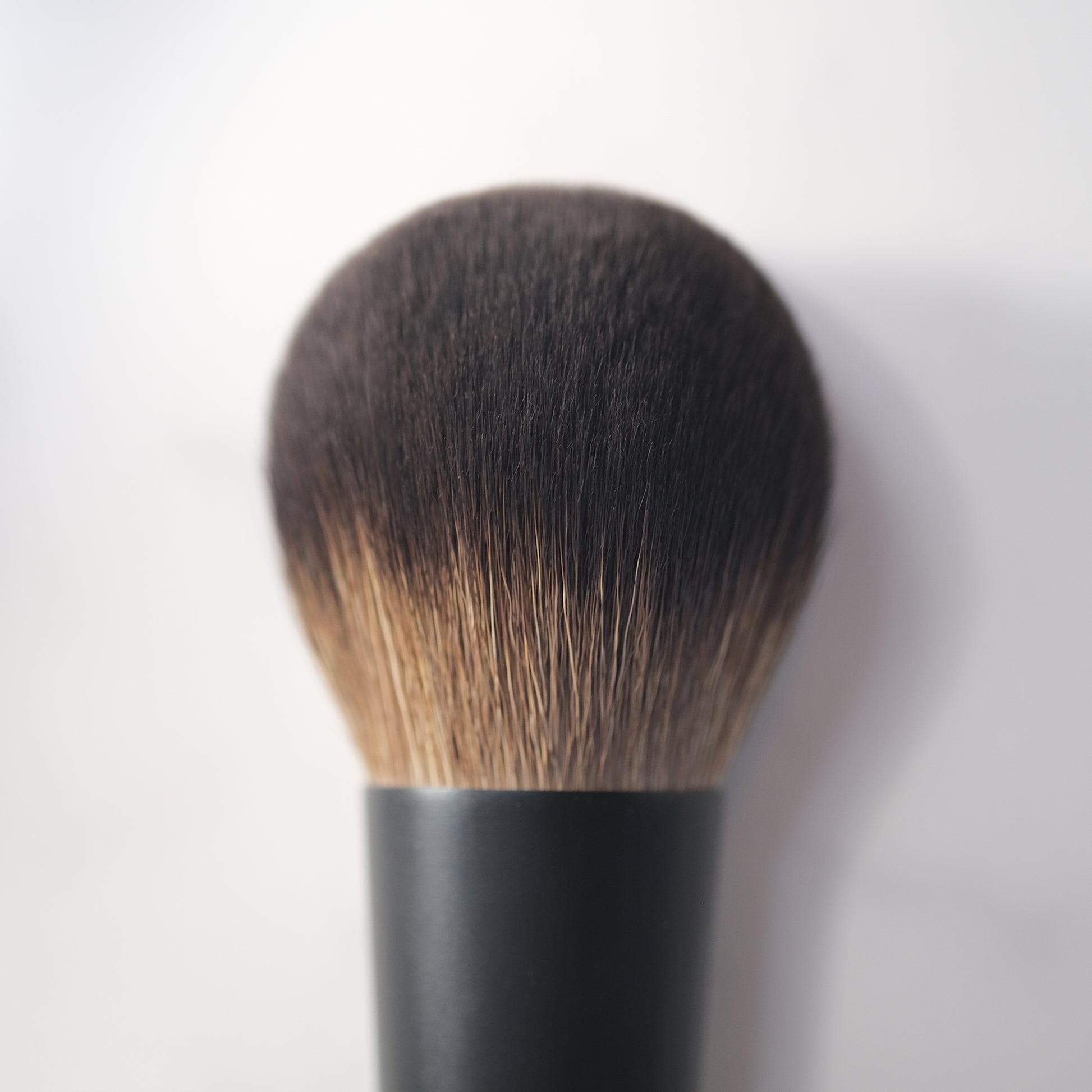 Makeup brush with black handle and brown bristles on a white background
