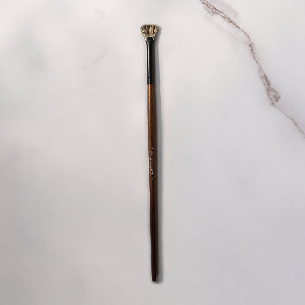 Makeup brush with wooden handle on a light gray background