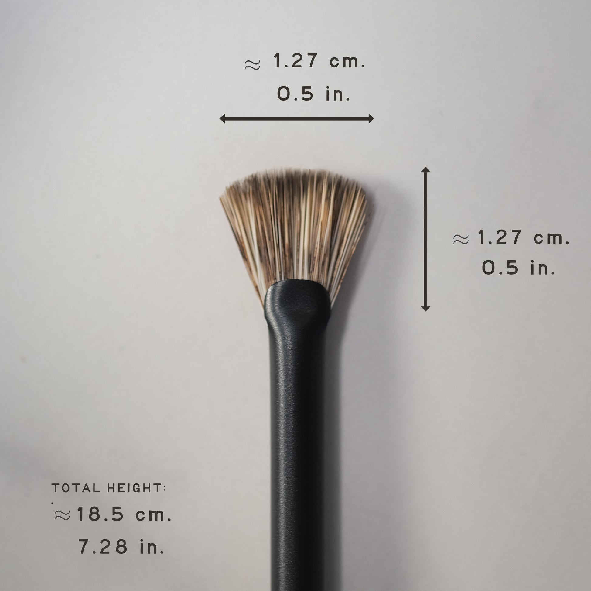 Black makeup brush with measurements on a gray background