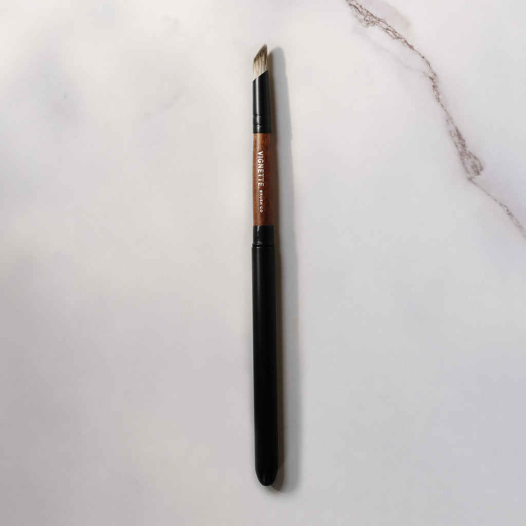 Eyebrow brush with black handle and brown bristle head on a light gray background