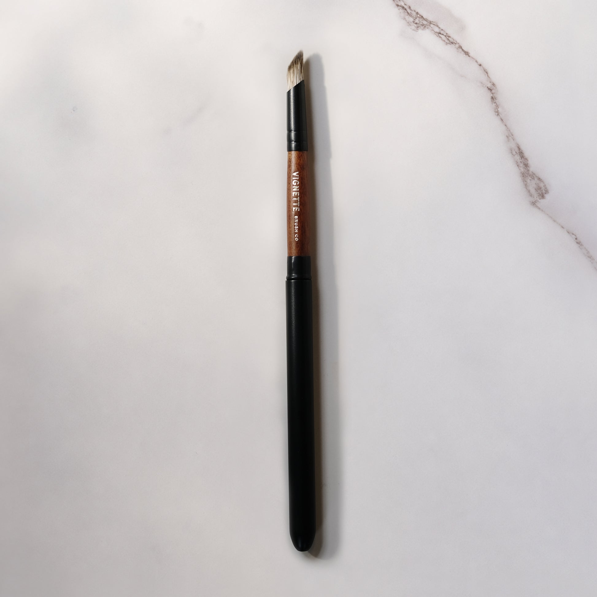 Eyebrow brush with black handle and brown bristle head on a light gray background