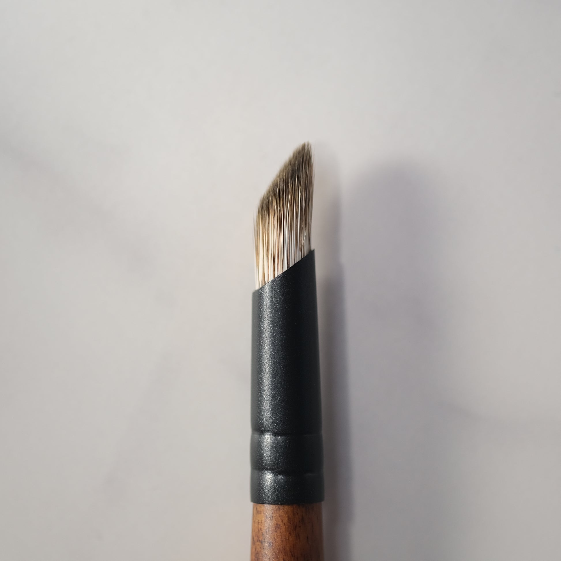Makeup brush with wooden handle and black ferrule on a light gray background