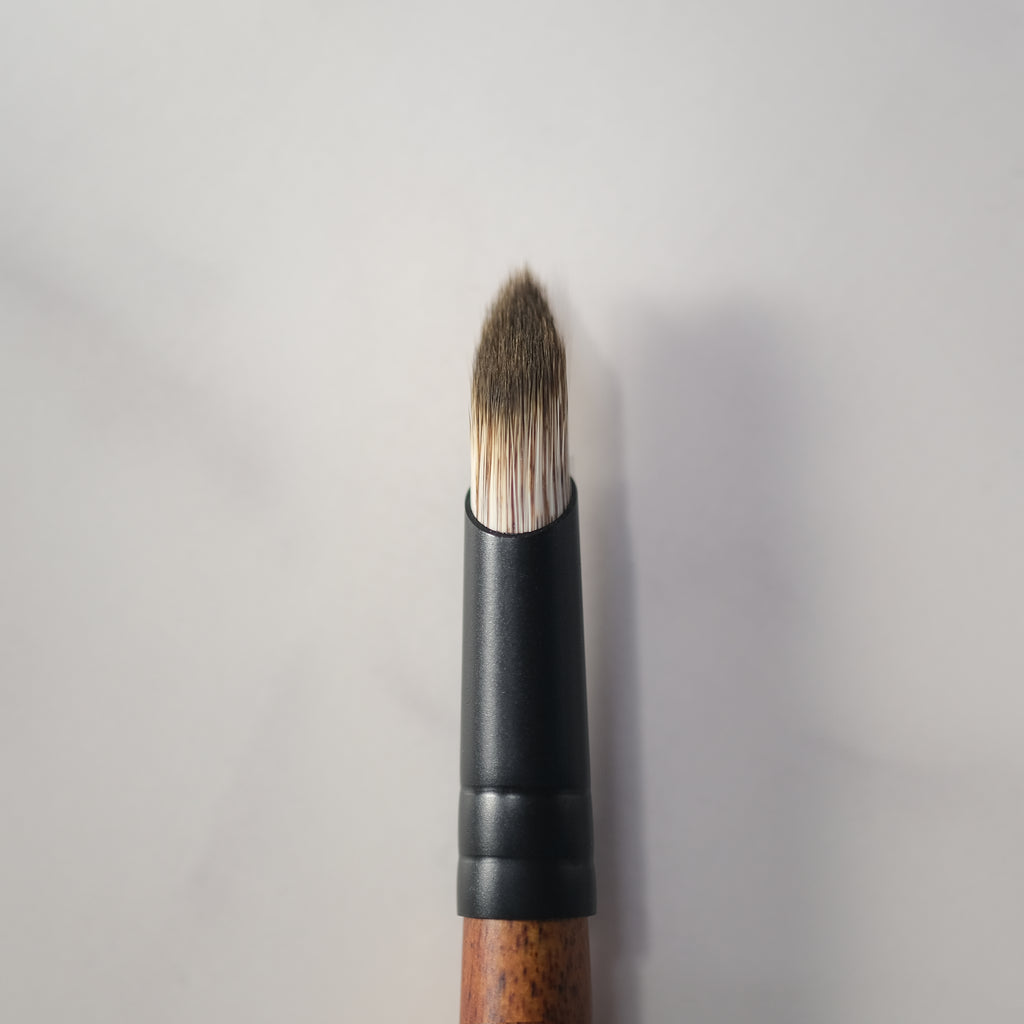 Makeup brush with black handle and wooden ferrule on a light gray background