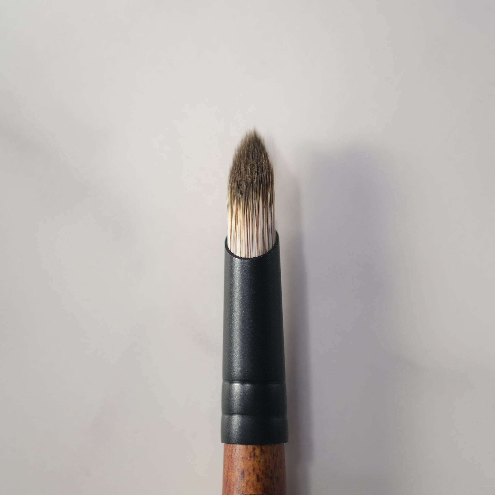 Makeup brush with black handle and wooden ferrule on a light gray background