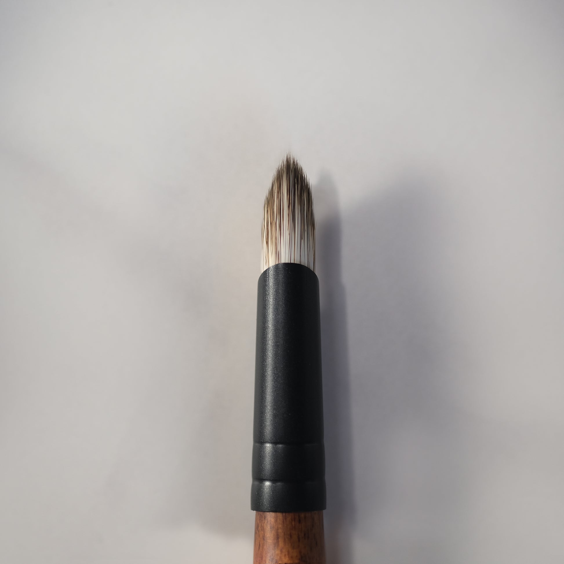 Makeup brush with black handle and wooden ferrule on a light gray background