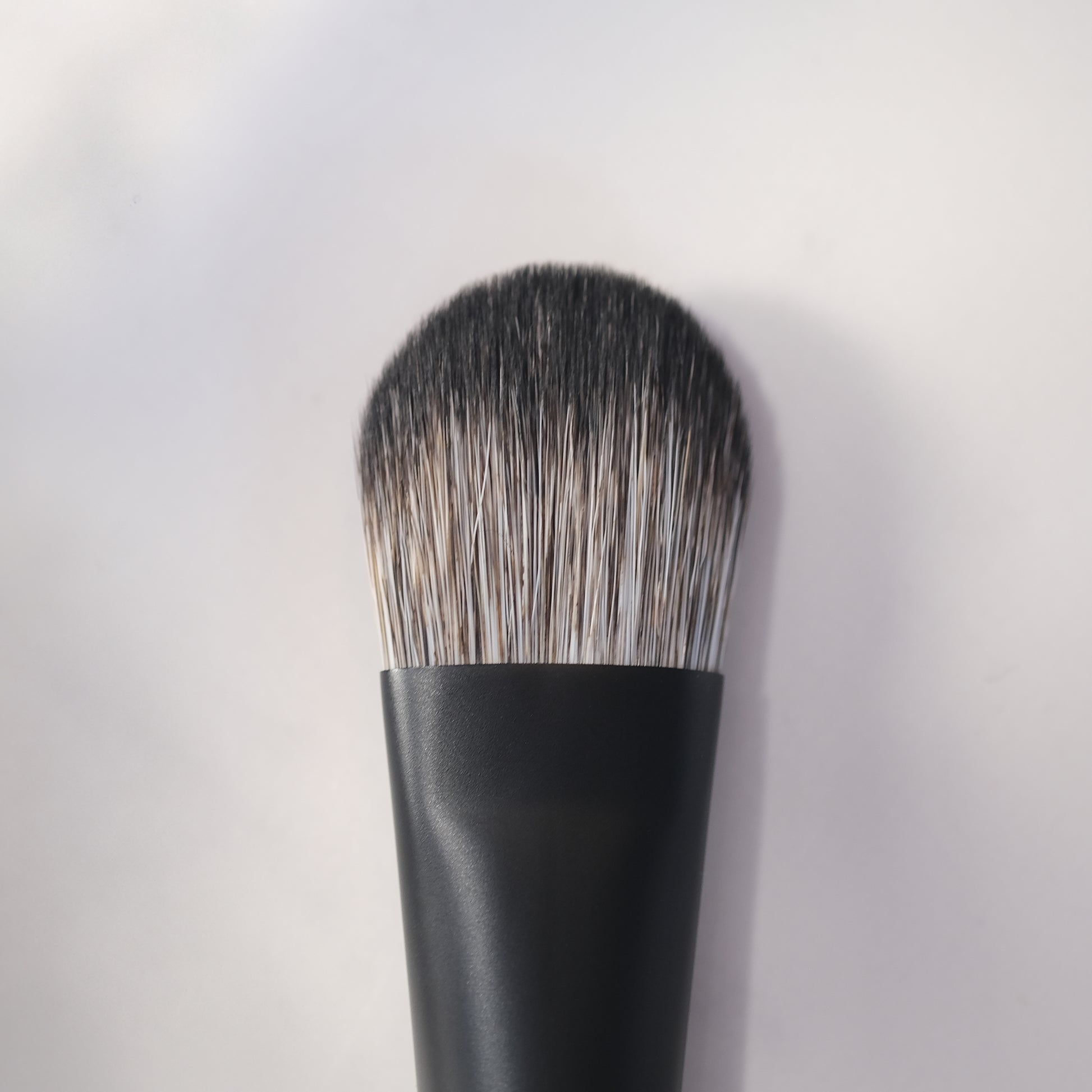 Makeup brush with black handle and bristles on a light gray background