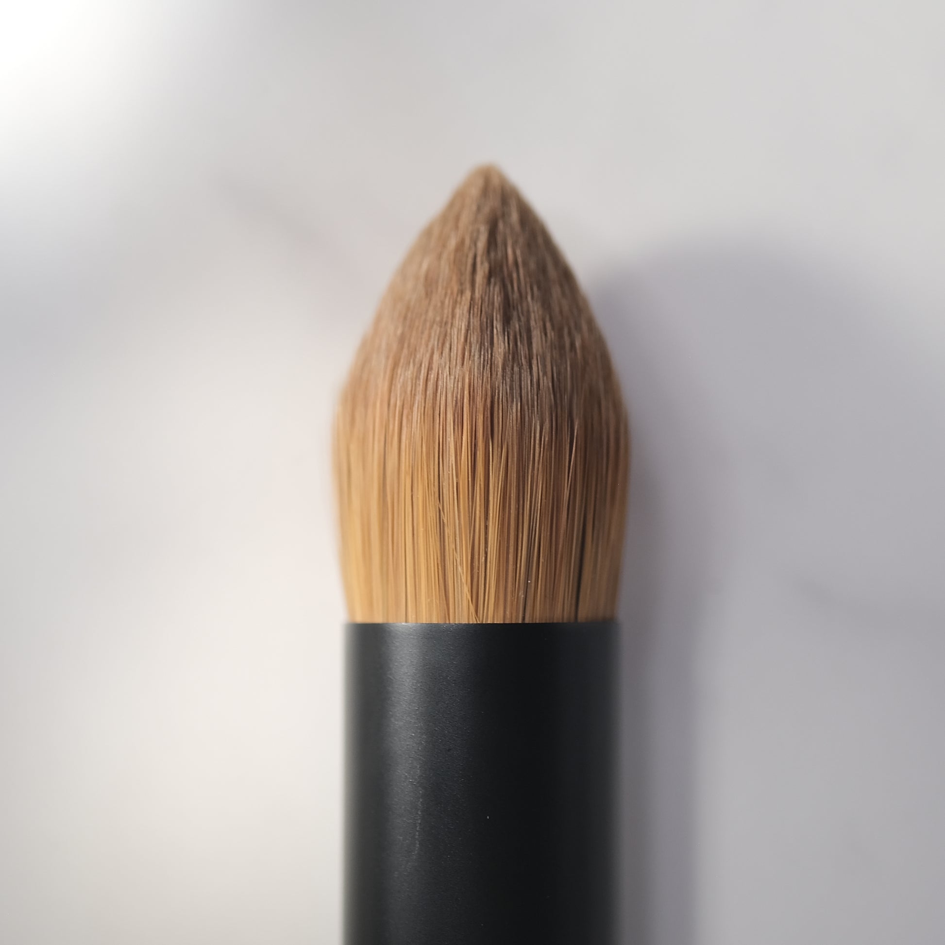Makeup brush with black handle and brown bristles on a white background