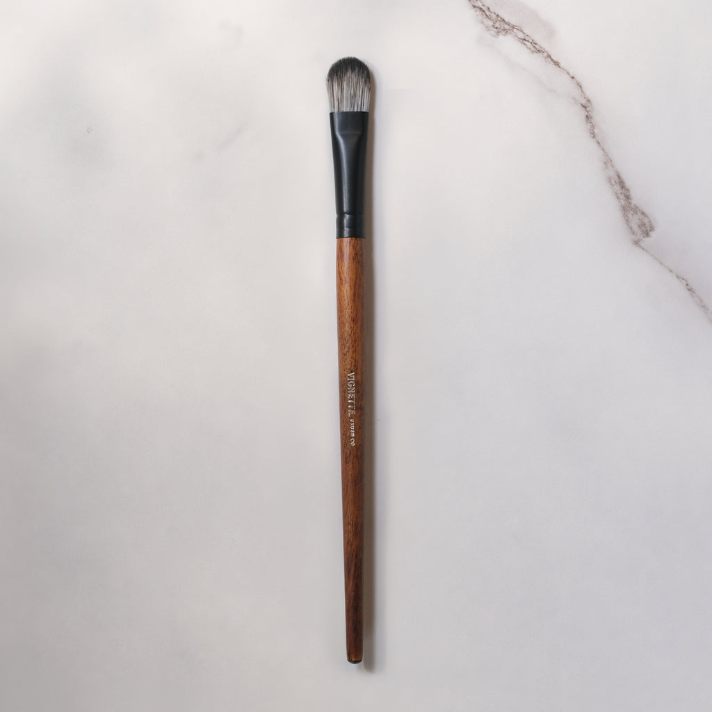 Makeup brush with wooden handle and black ferrule on a light gray background