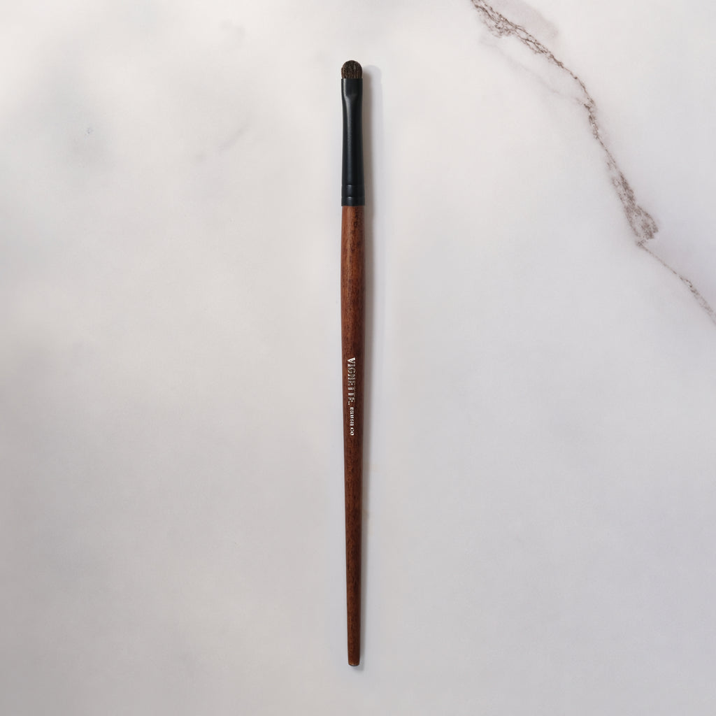 Makeup brush with wooden handle and black ferrule on a light gray background