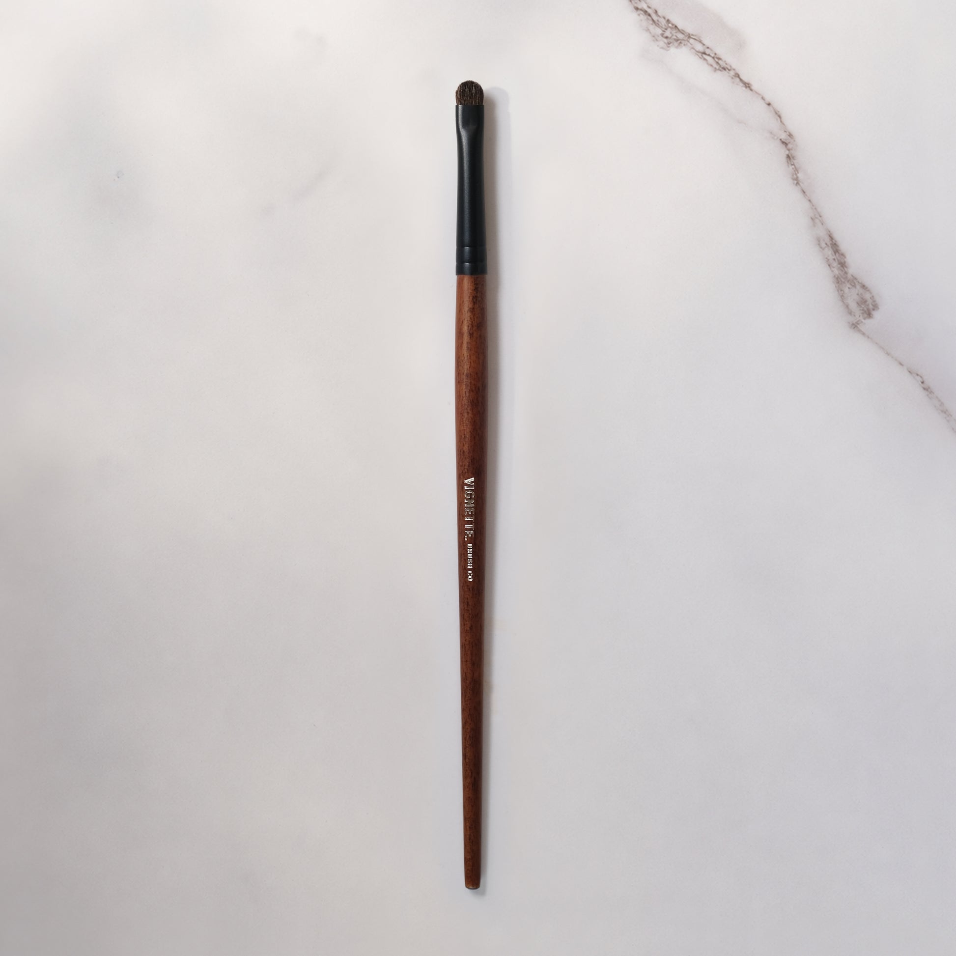 Makeup brush with wooden handle and black ferrule on a light gray background