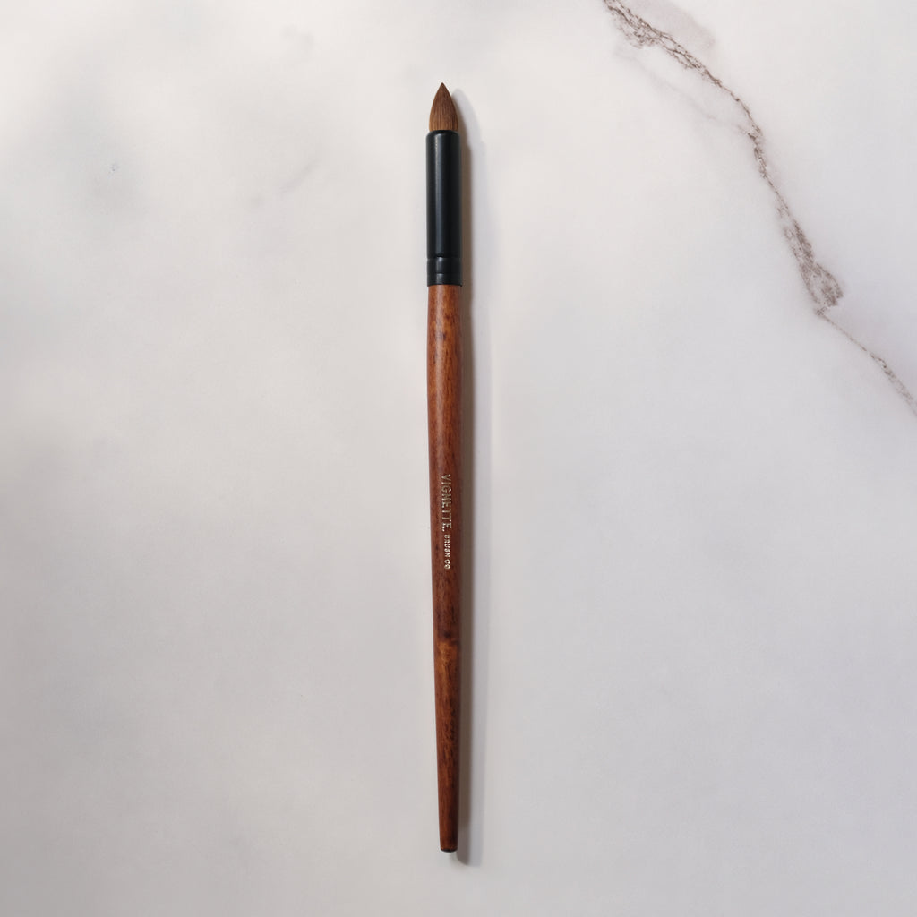 Wooden makeup brush with black ferrule on a light gray background