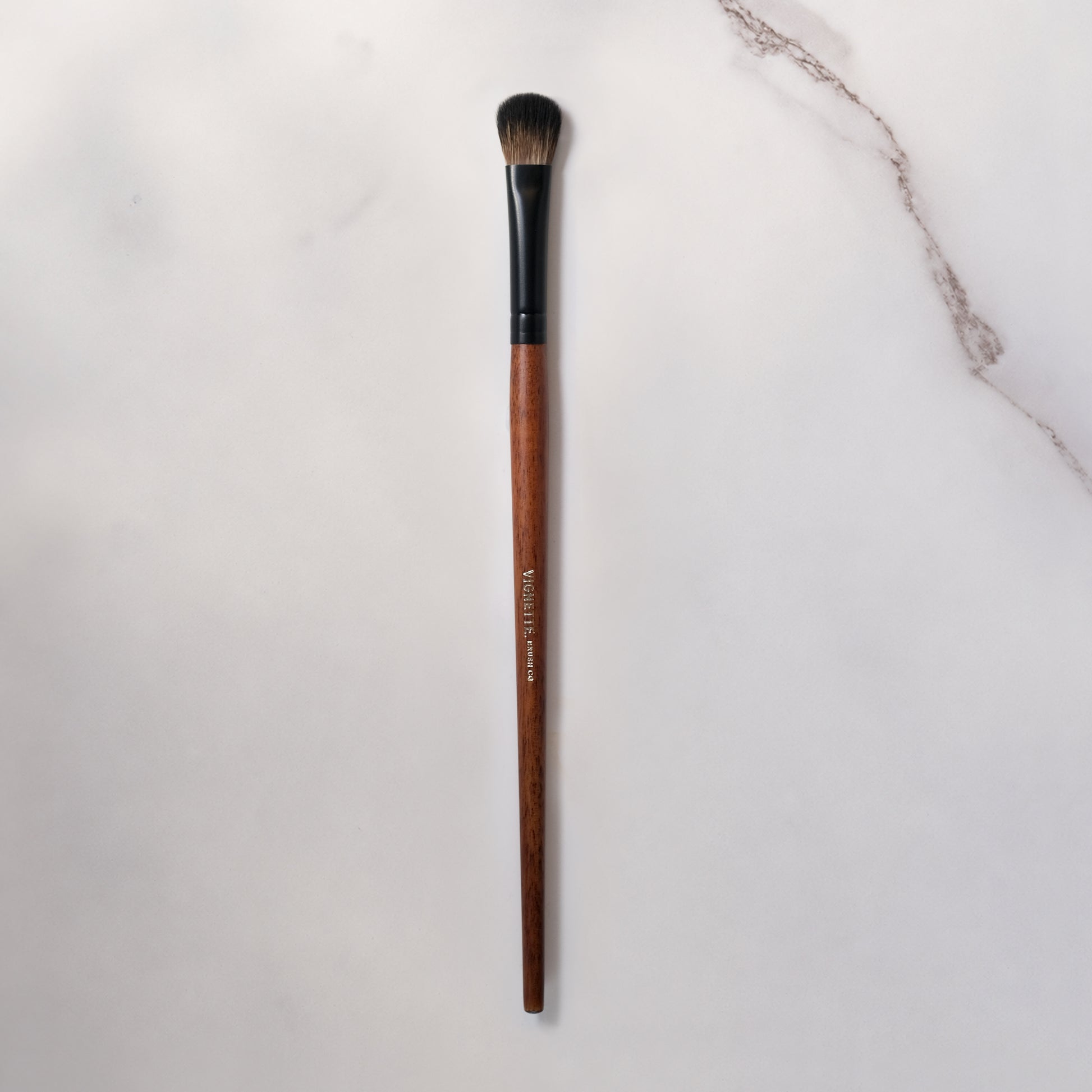 Makeup brush with brown handle and black ferrule on a light gray background