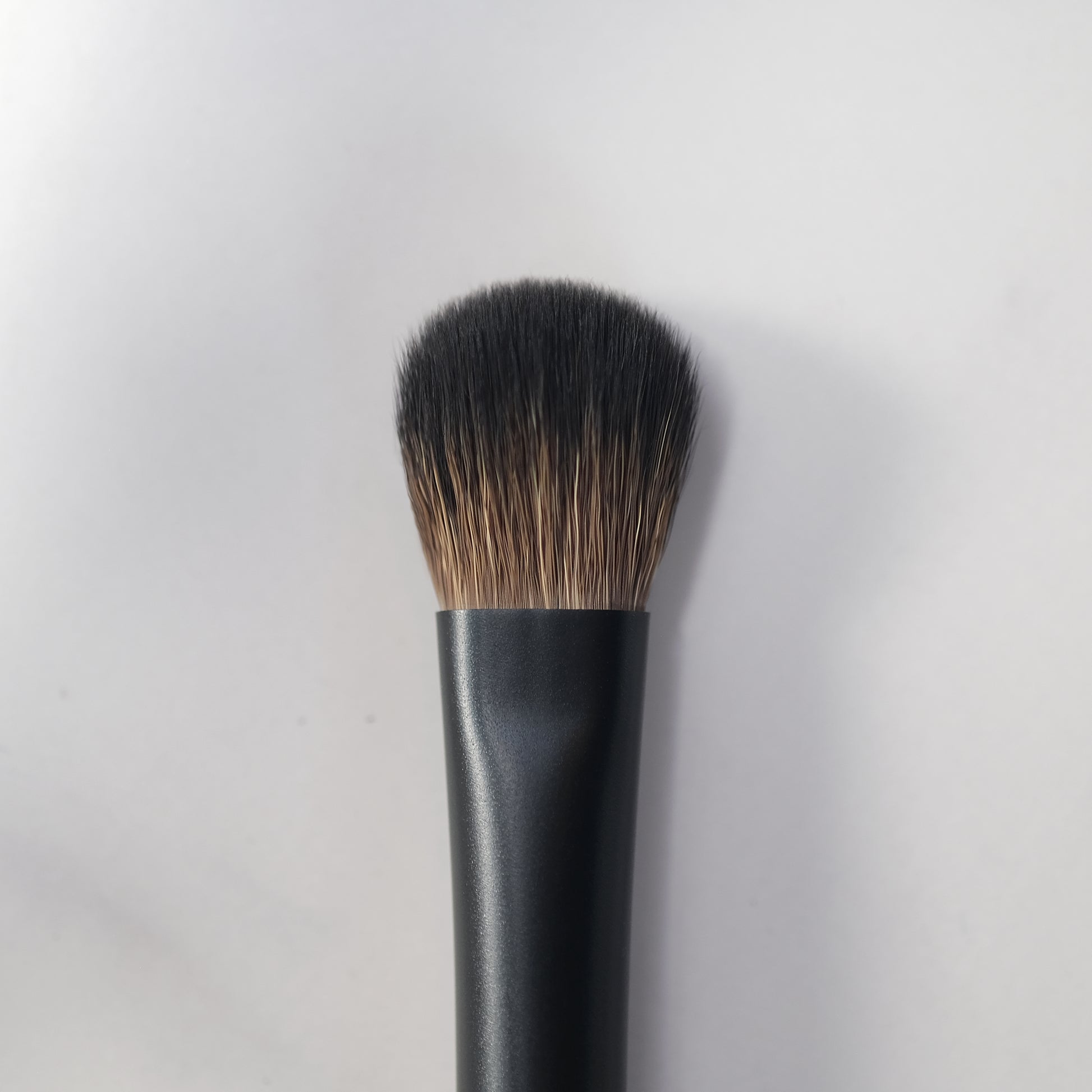 Makeup brush with black handle and bristles on a light gray background