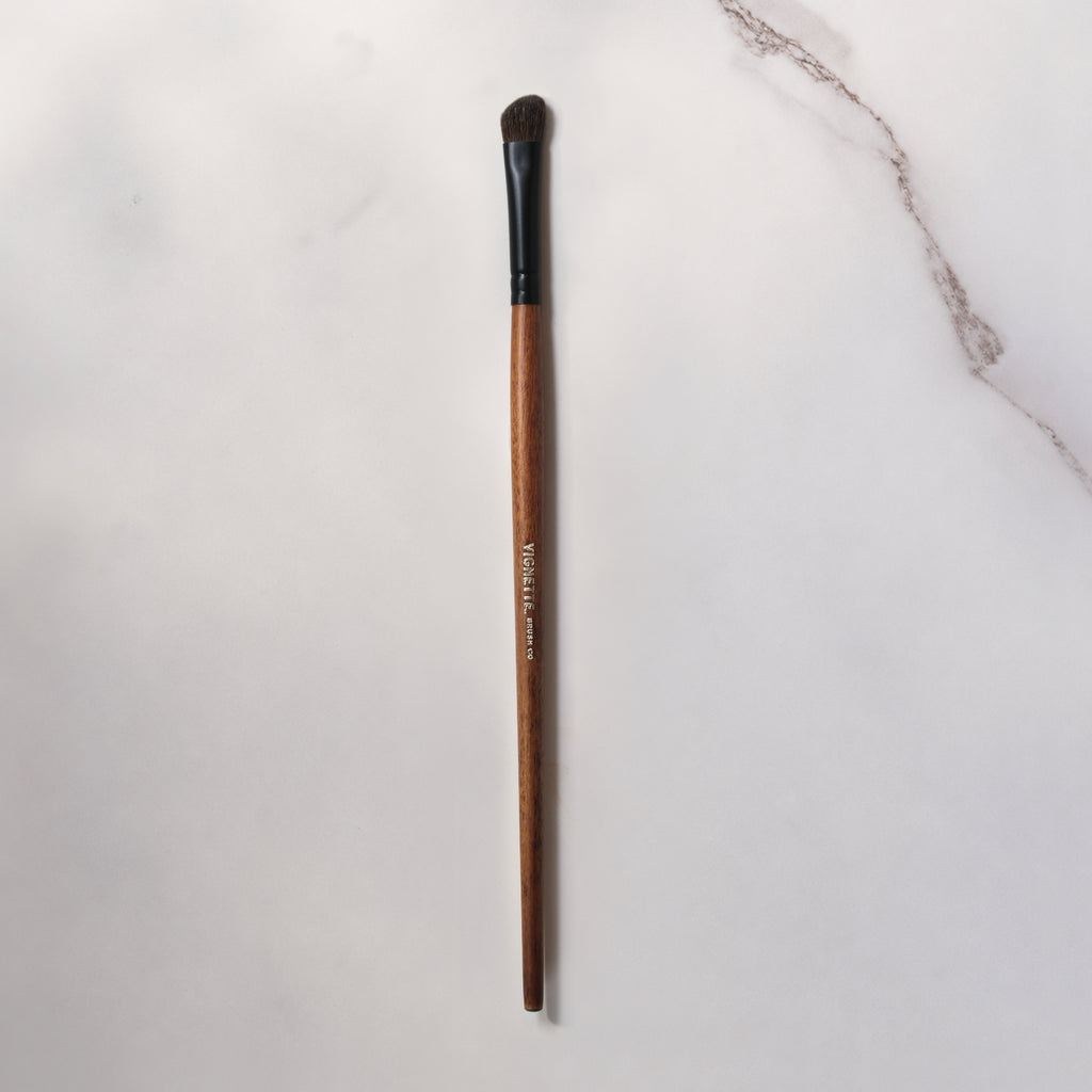 Makeup brush with wooden handle and black ferrule on a light gray background