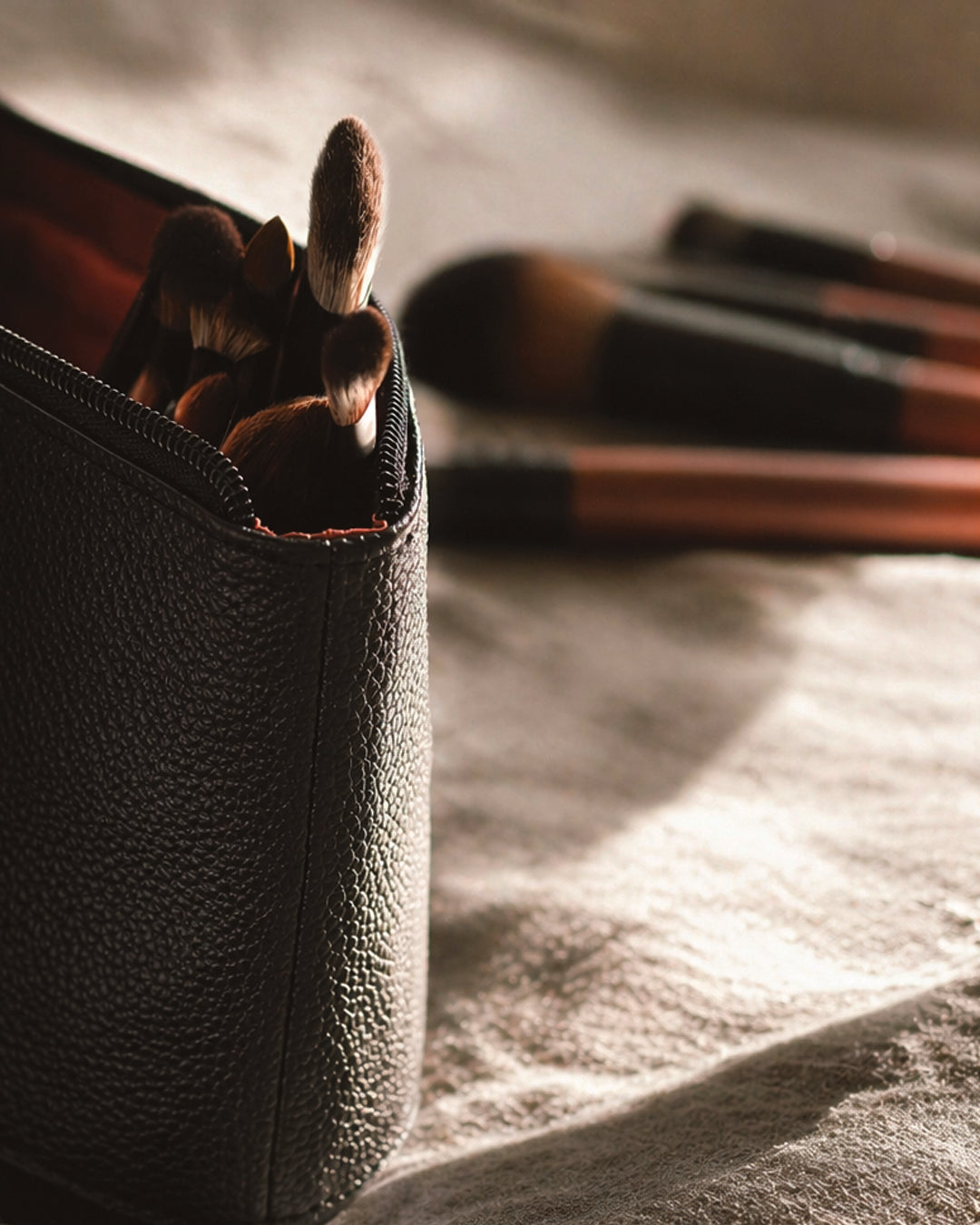 Makeup brushes in a black leather case on a textured surface