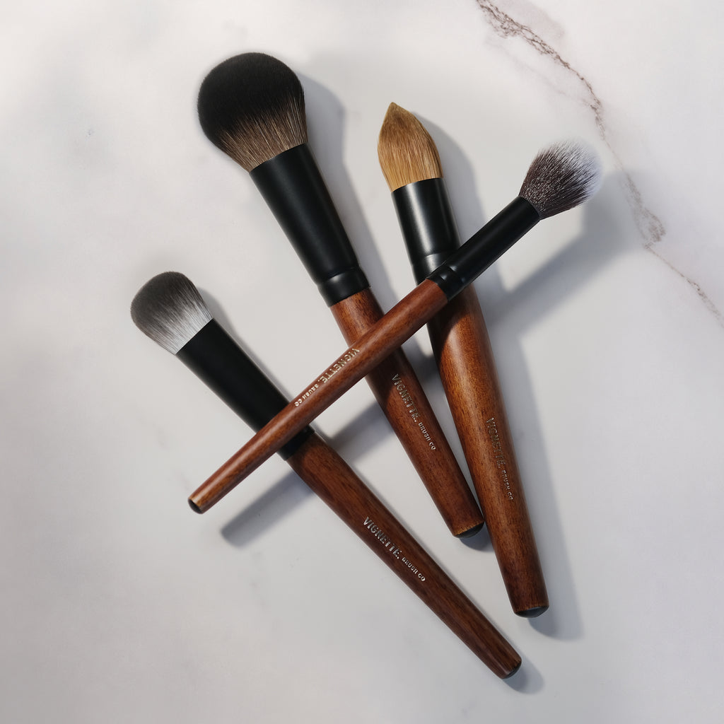 Set of makeup brushes with wooden handles and black ferrules on a light background