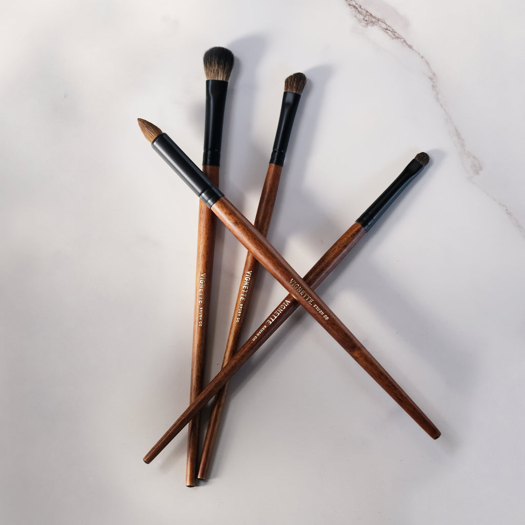 Set of makeup brushes with wooden handles and black ferrules on a light marble background