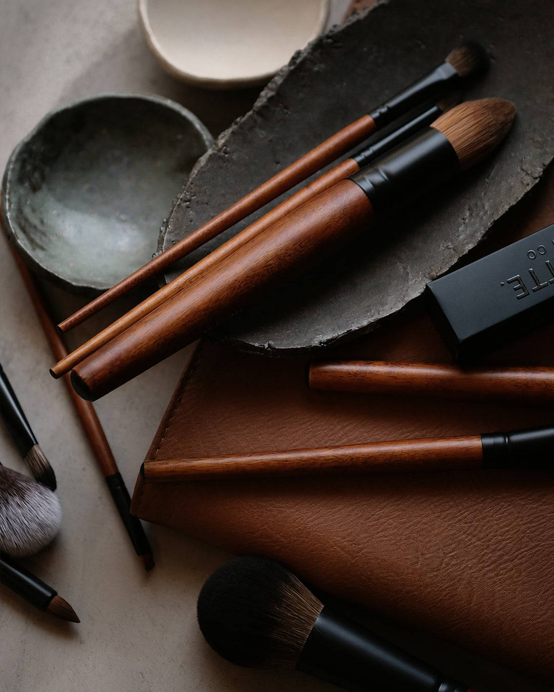 Makeup brushes on a textured surface with a brand name visible