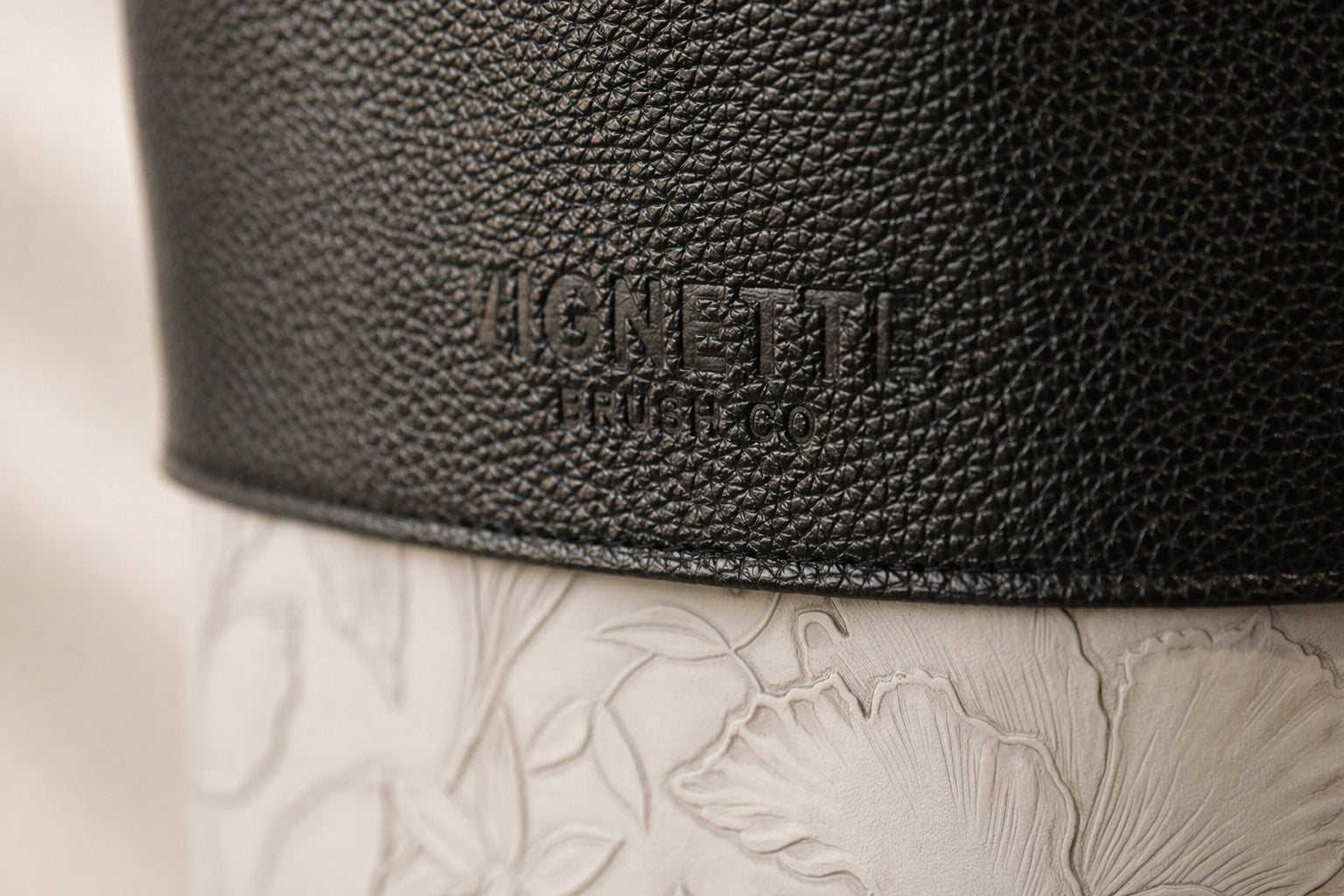 Close-up of a black leather product with 'Hermès' branding on a beige background.