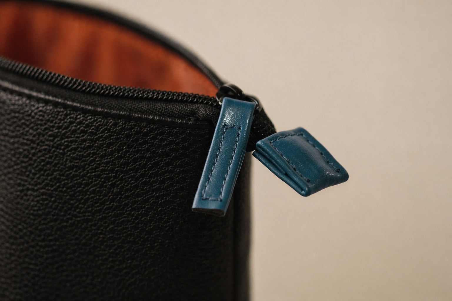 Close-up of a black leather pouch with blue zipper tab on a beige background