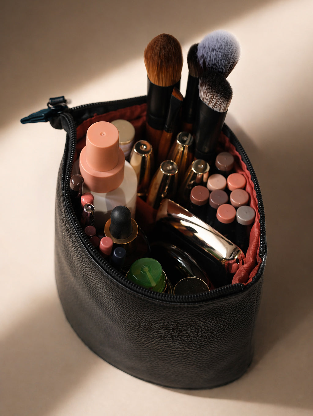 Makeup bag with various cosmetic items including brushes and bottles on a neutral background