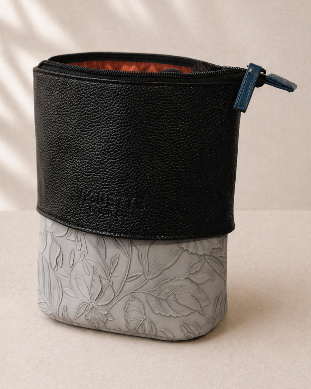 Two-tone pouch with black top and gray bottom with leaf pattern on a beige background