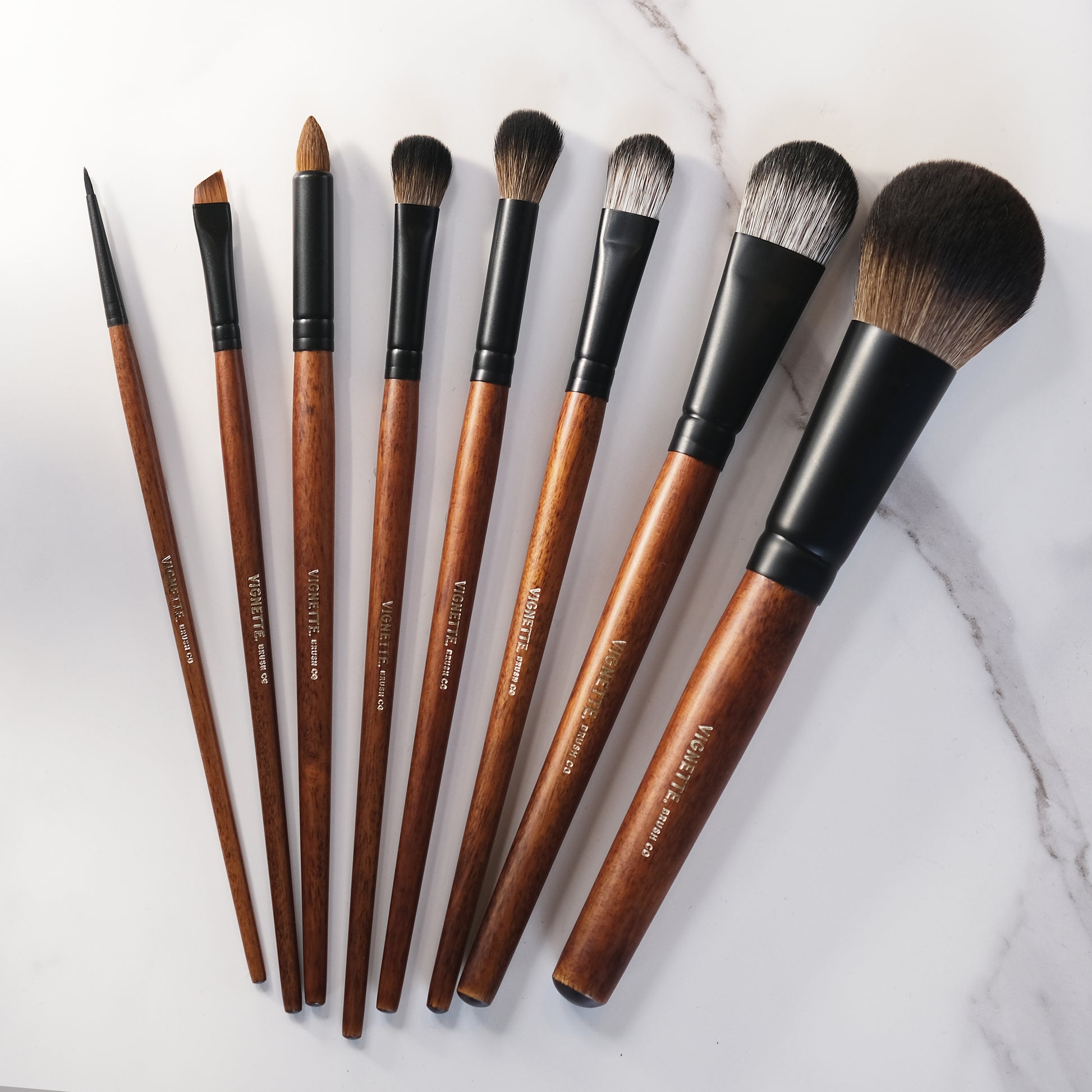 Set of makeup brushes with brown handles and black ferrules on a marble surface