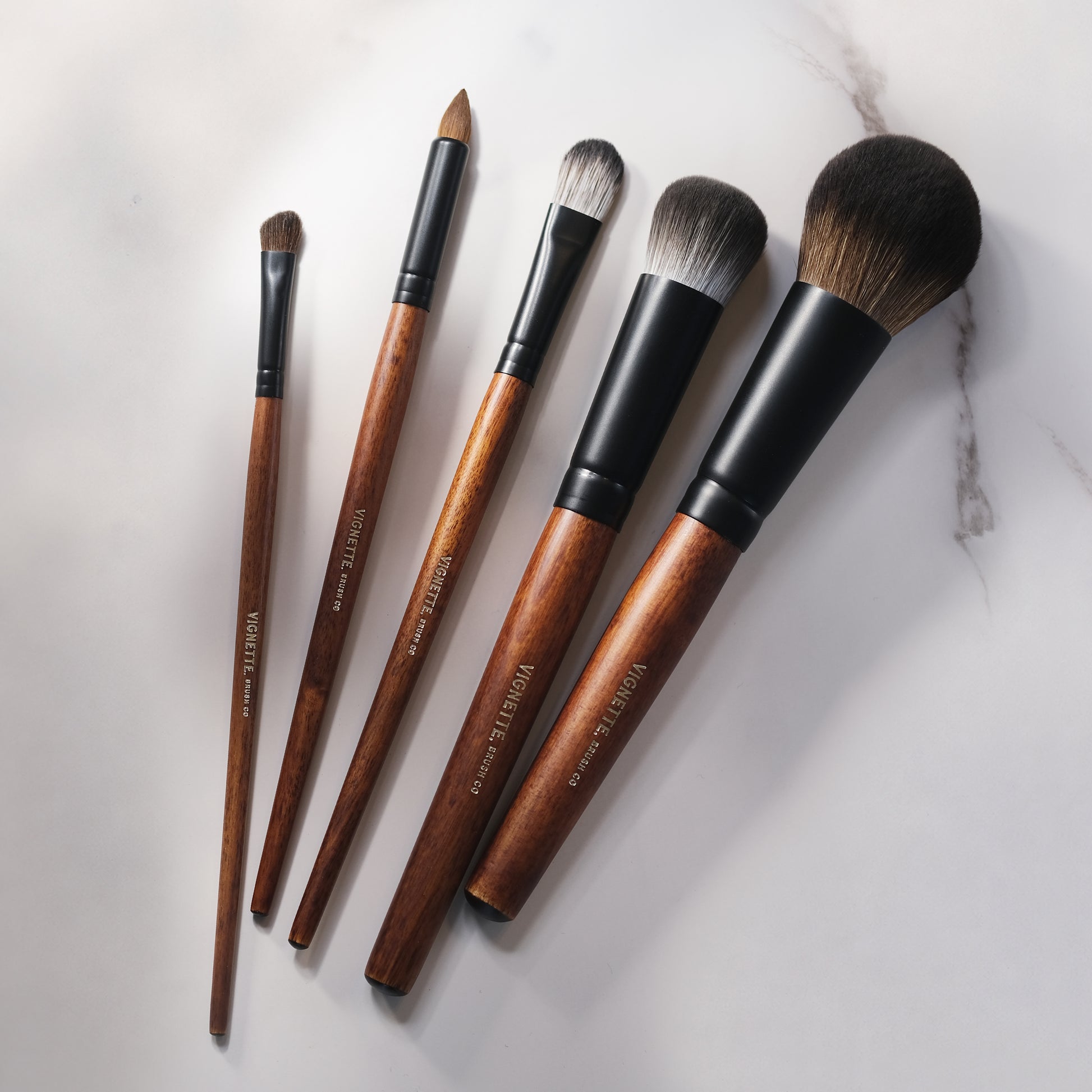 Set of makeup brushes with wooden handles and black ferrules on a light background